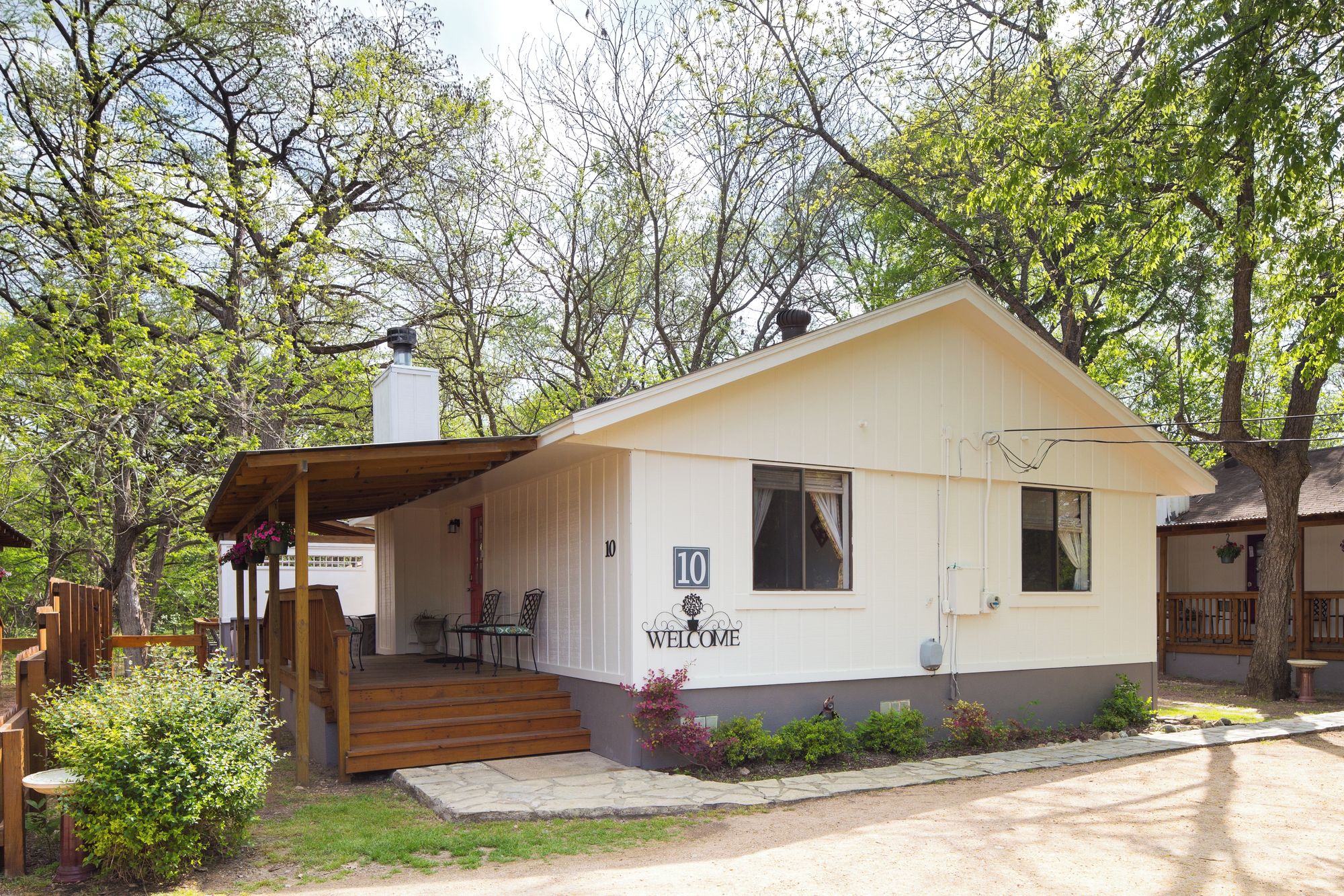 A small, single-story cabin with a porch, a chimney, and a welcome sign.