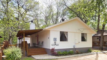 A small, single-story cabin with a porch, a chimney, and a welcome sign.
