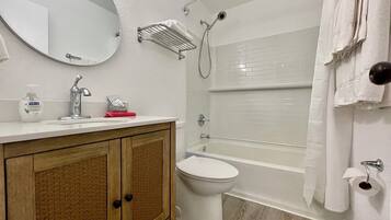 A bathroom with a wooden vanity, a toilet, a bathtub, and a shower.
