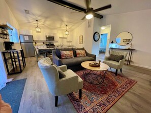 Una sala de estar moderna con un sofá, sillones, una mesa de centro y una cocina al fondo.