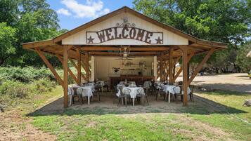 Un pavillon en bois avec une pancarte indiquant « BIENVENUE », des tables recouvertes de nappes blanches et un espace cuisine.