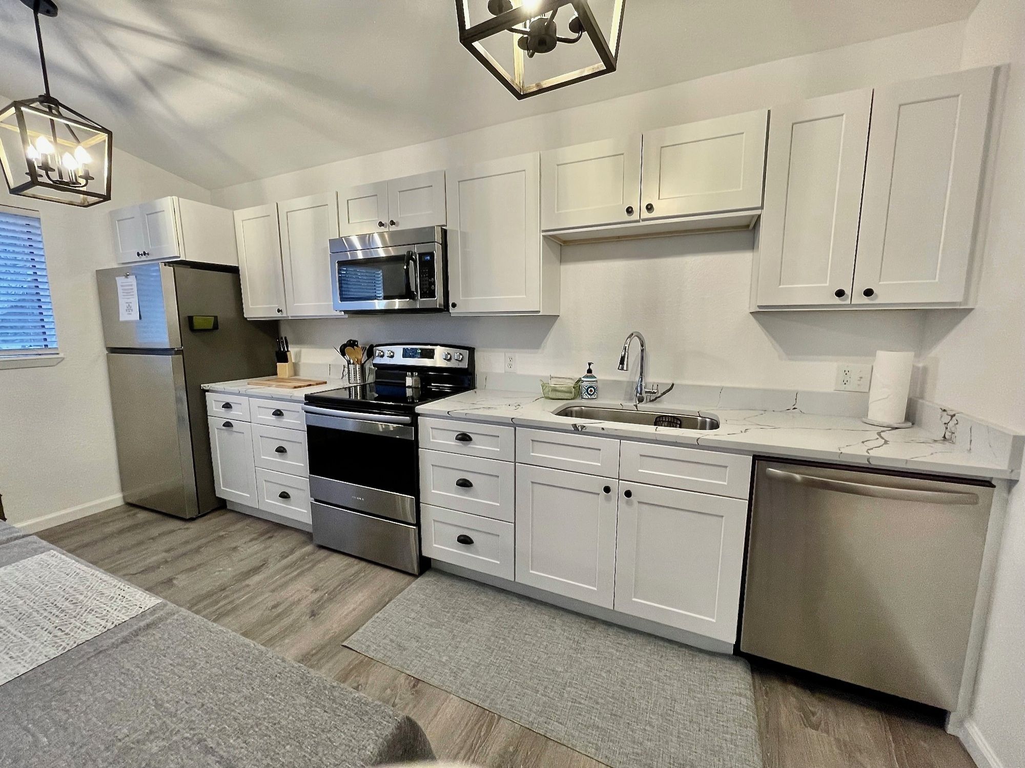 A modern kitchen with white cabinets, stainless steel appliances, and a marble countertop.