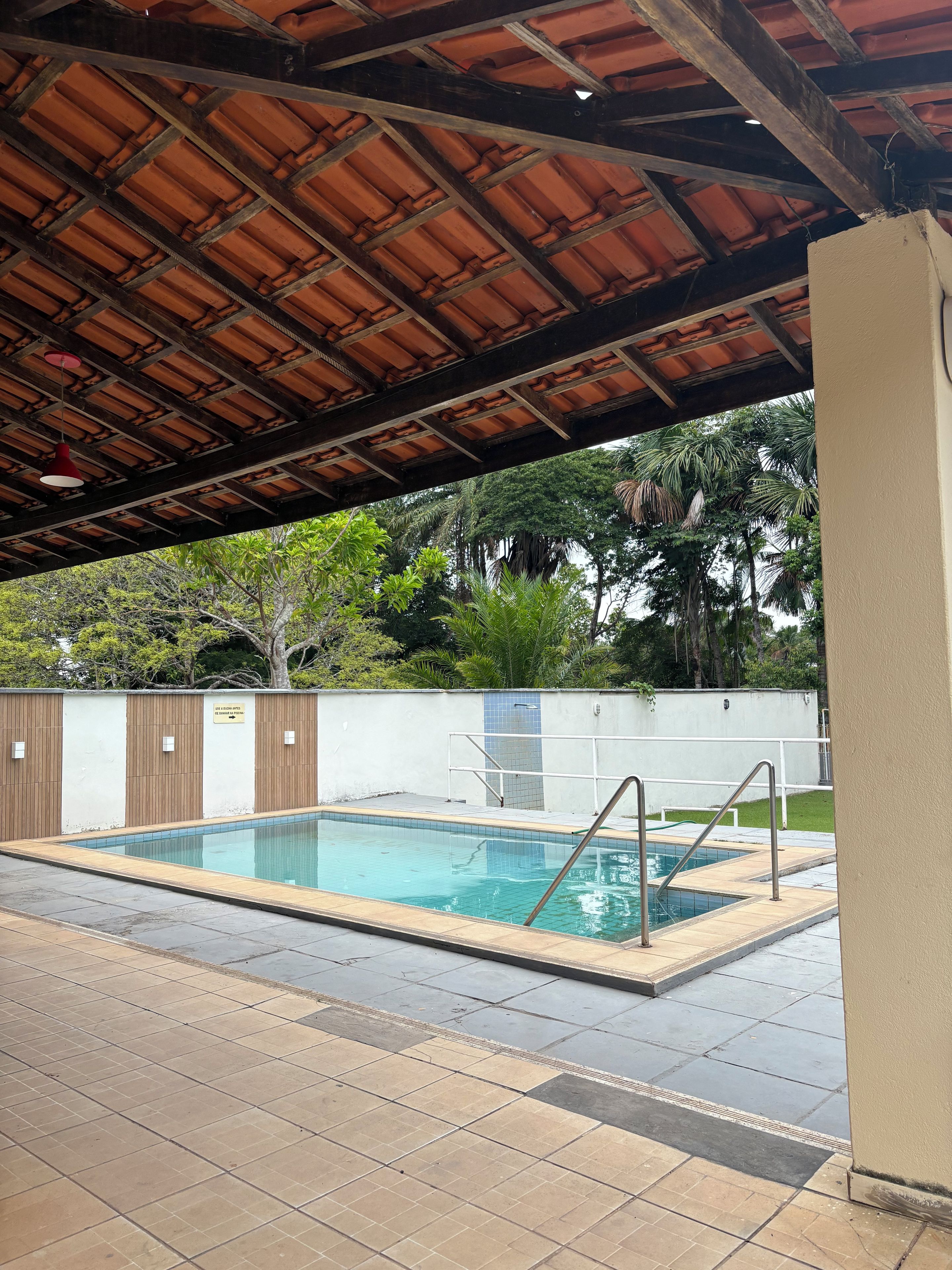 An outdoor swimming pool with a tiled deck, a wooden ceiling, and a white wall with a sign.
