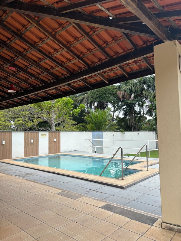 An outdoor swimming pool with a tiled deck, a wooden ceiling, and a white wall with a sign.