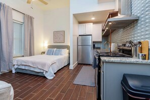 A compact hotel room with a bed, a small kitchenette, and a bathroom. - Downtown Extended Stay Studio (Wichita)