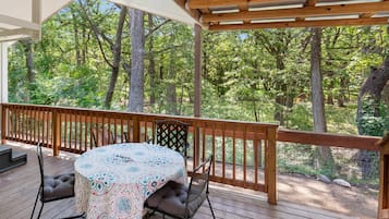 An outdoor deck with a table and chairs, surrounded by a wooden railing, overlooking a forested area.