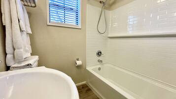 A bathroom with a white bathtub, a toilet, a towel rack, and a window with blinds.