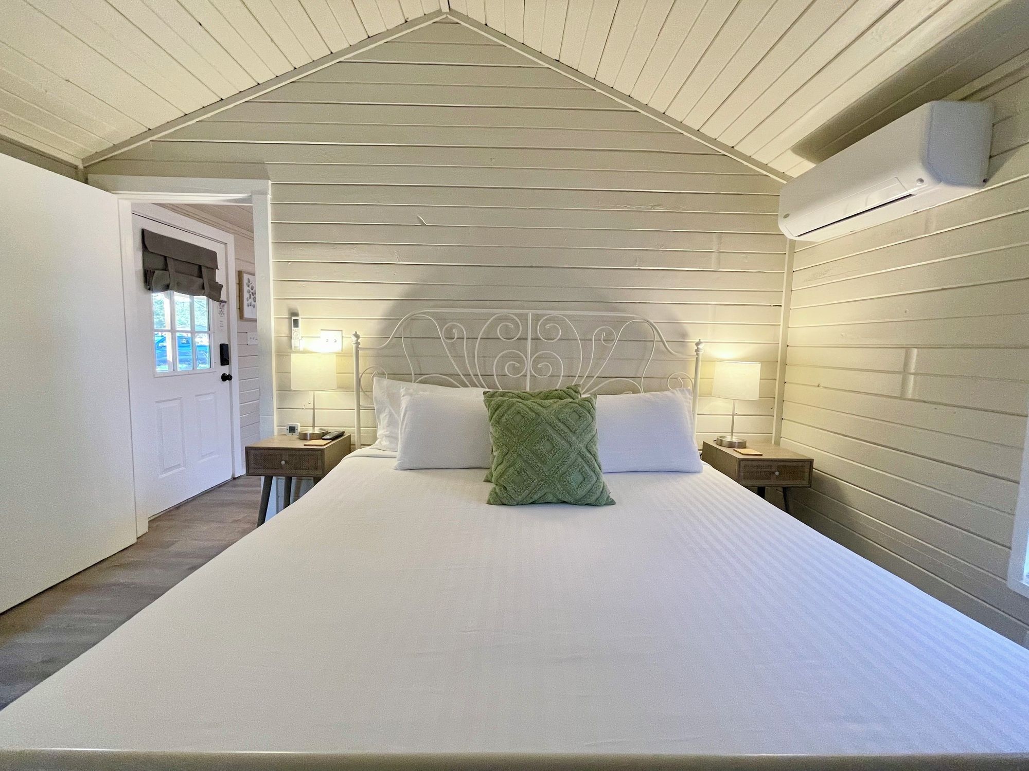 A bedroom with a bed, two bedside tables, a headboard, and a window with curtains.