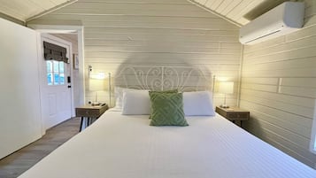 A bedroom with a bed, two bedside tables, a headboard, and a window with curtains.