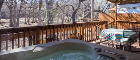 A hot tub with a wooden deck, a table with chairs, and a view of trees.