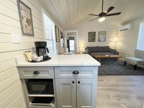 A kitchen with a coffee maker, a refrigerator, and a dining area with a couch and a table. - Cottage 12 Pewter, Pet-Friendly One-Bedroom Cottage, Private Hot Tub (Wimberley)