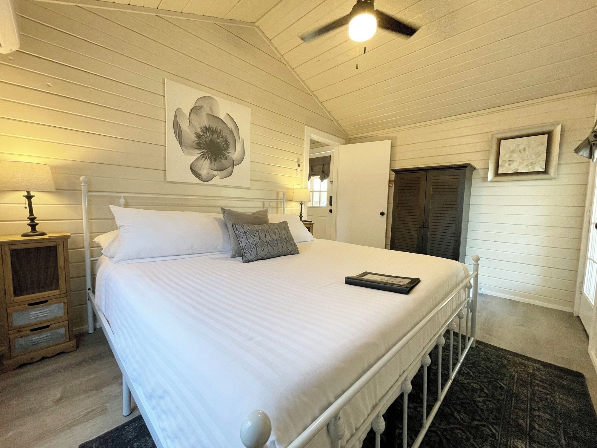 A bedroom with a bed, bedside lamps, a ceiling fan, and a door.
