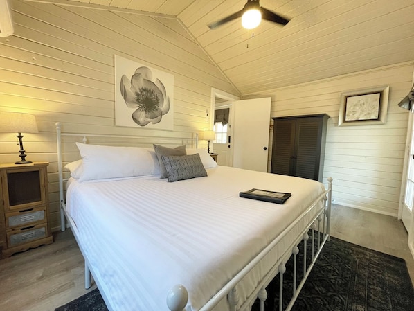 A bedroom with a bed, bedside lamps, a ceiling fan, and a door. - Cottage 12 Pewter, Pet-Friendly One-Bedroom Cottage, Private Hot Tub (Wimberley)