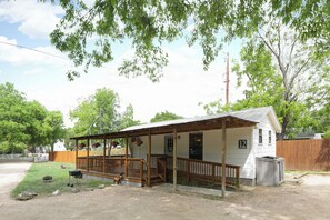 A single-story house with a porch, a fenced yard, and a number '12' sign. - Cottage 12 Pewter, Pet-Friendly One-Bedroom Cottage, Private Hot Tub (Wimberley)