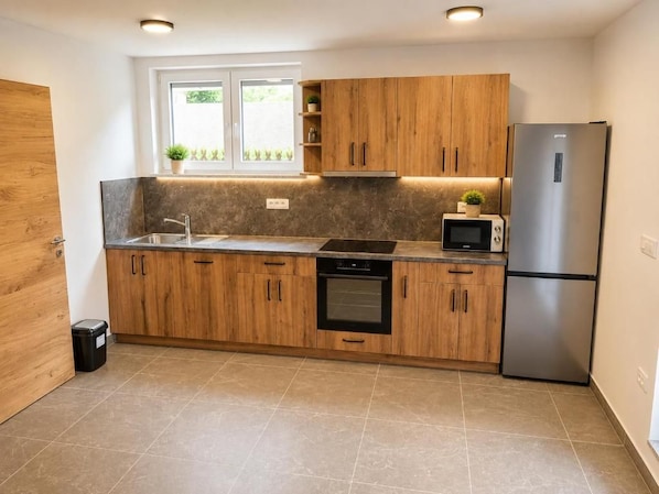 A modern kitchen with wooden cabinets, a stainless steel refrigerator, a microwave, and a built-in oven.