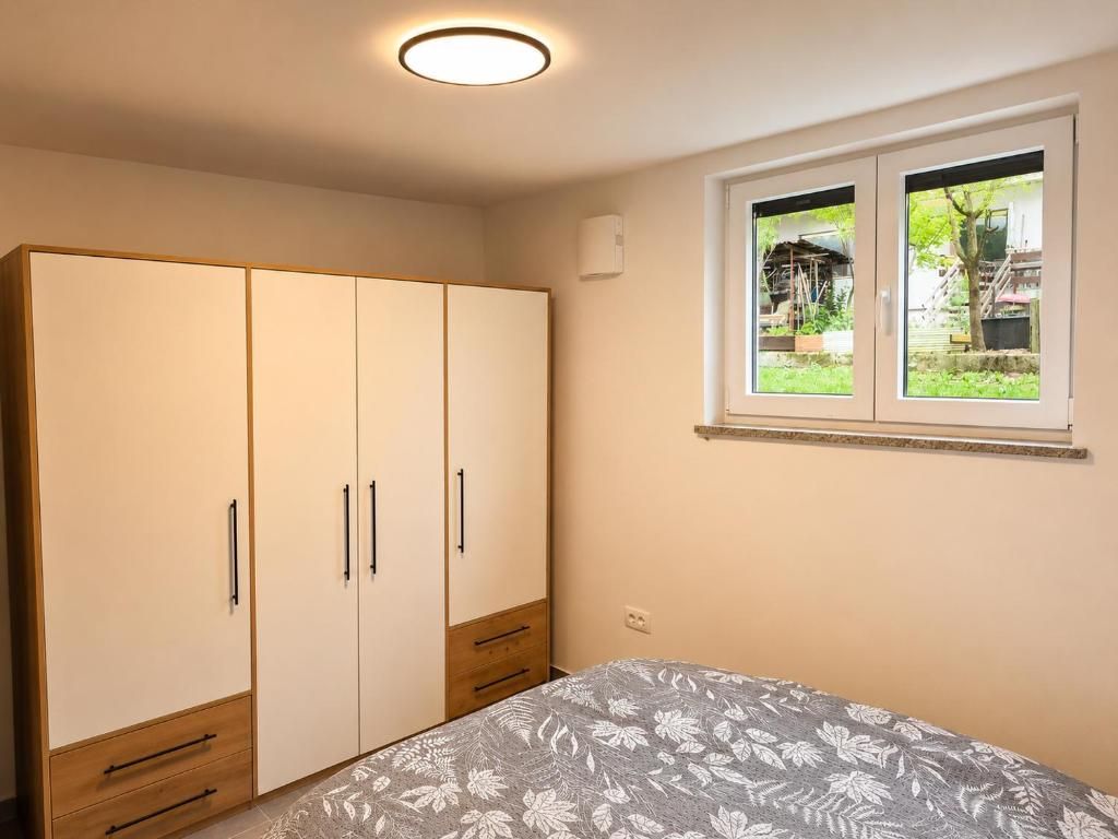 A bedroom with a bed, a wardrobe, and a window with a view of greenery.