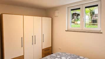 A bedroom with a bed, a wardrobe, and a window with a view of greenery.