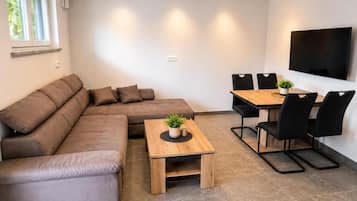 A modern living room with a sectional sofa, a wooden coffee table, and a dining area with chairs and a TV.