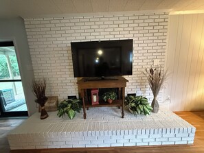 A flat-screen TV on a wooden stand against a white brick wall. - GUNILLA's VILLA - The heart of downtown with privacy near LAKE NORMAN (Mooresville)