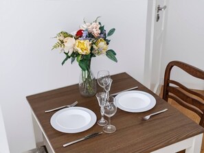 A dining table set with white plates, cutlery, and wine glasses, accompanied by a vase of flowers. - Warsaw Old Town Studio — Top Location (Warszawa)