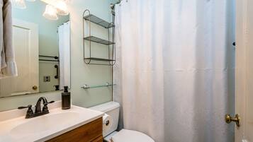 Un baño con lavamanos blanco, espejo, toallero, inodoro y cortina de ducha.