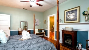 A bedroom with a four-poster bed, a fireplace, and a door leading to another room.