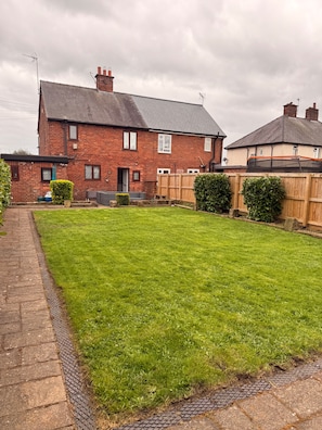 A residential property with a well-maintained lawn, a brick house, and a wooden fence. - House Sleeps 7 with Garden and Parking (Chester)