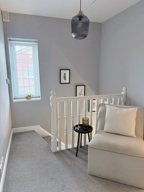 A room with a white railing, a grey sofa, a small table with a vase, and a hanging light fixture. - House Sleeps 7 with Garden and Parking (Chester)