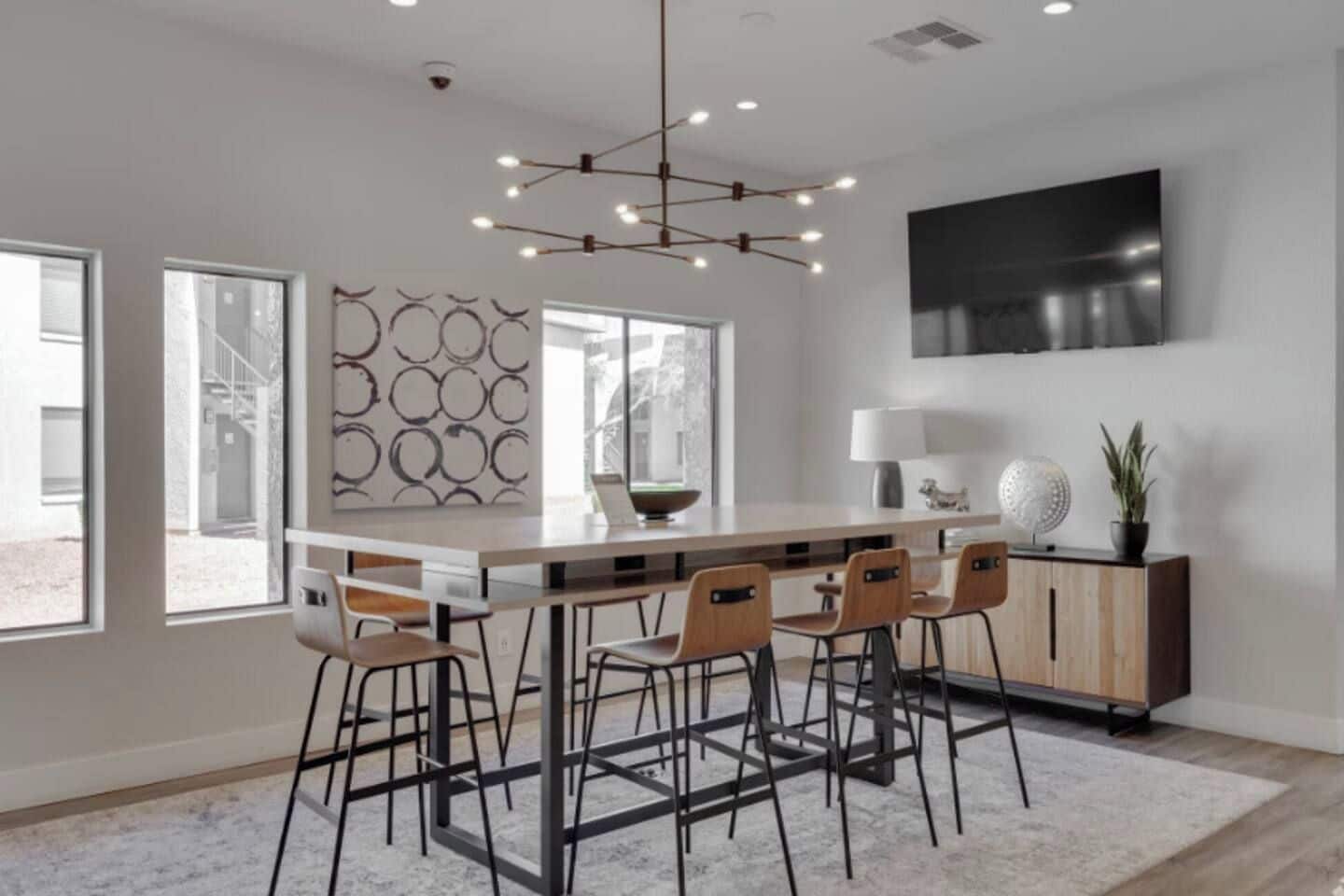 Una cocina moderna con una isla central, taburetes de bar, una mesa de comedor y un televisor montado en la pared.