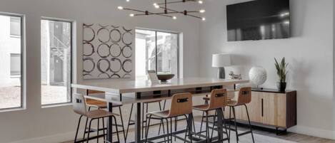 A modern kitchen with a central island, bar stools, a dining table, and a TV mounted on the wall.