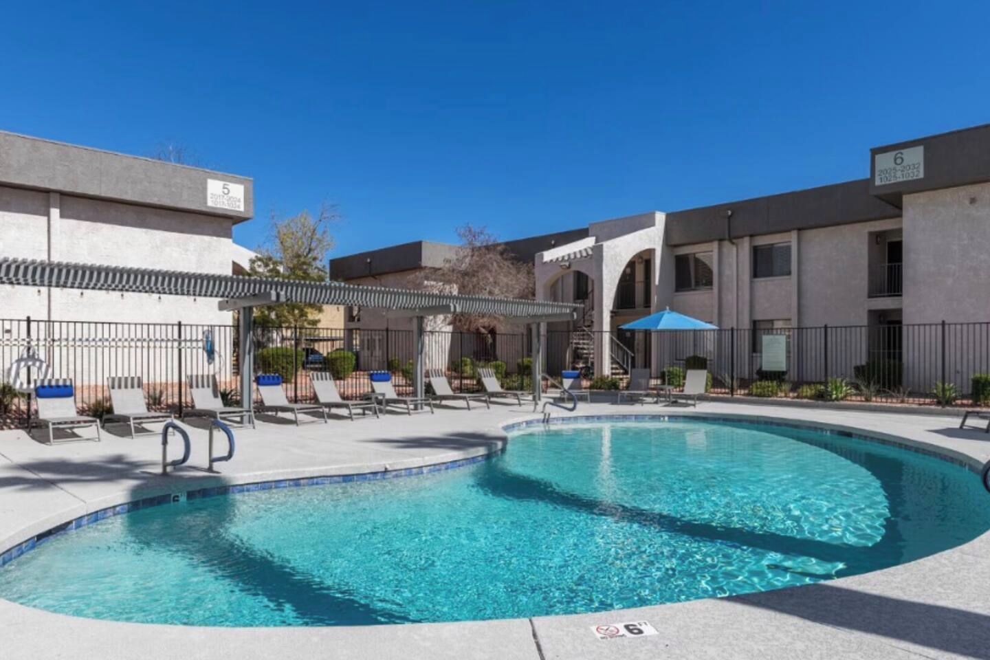 A swimming pool with lounge chairs and umbrellas, surrounded by buildings with numbered signs.