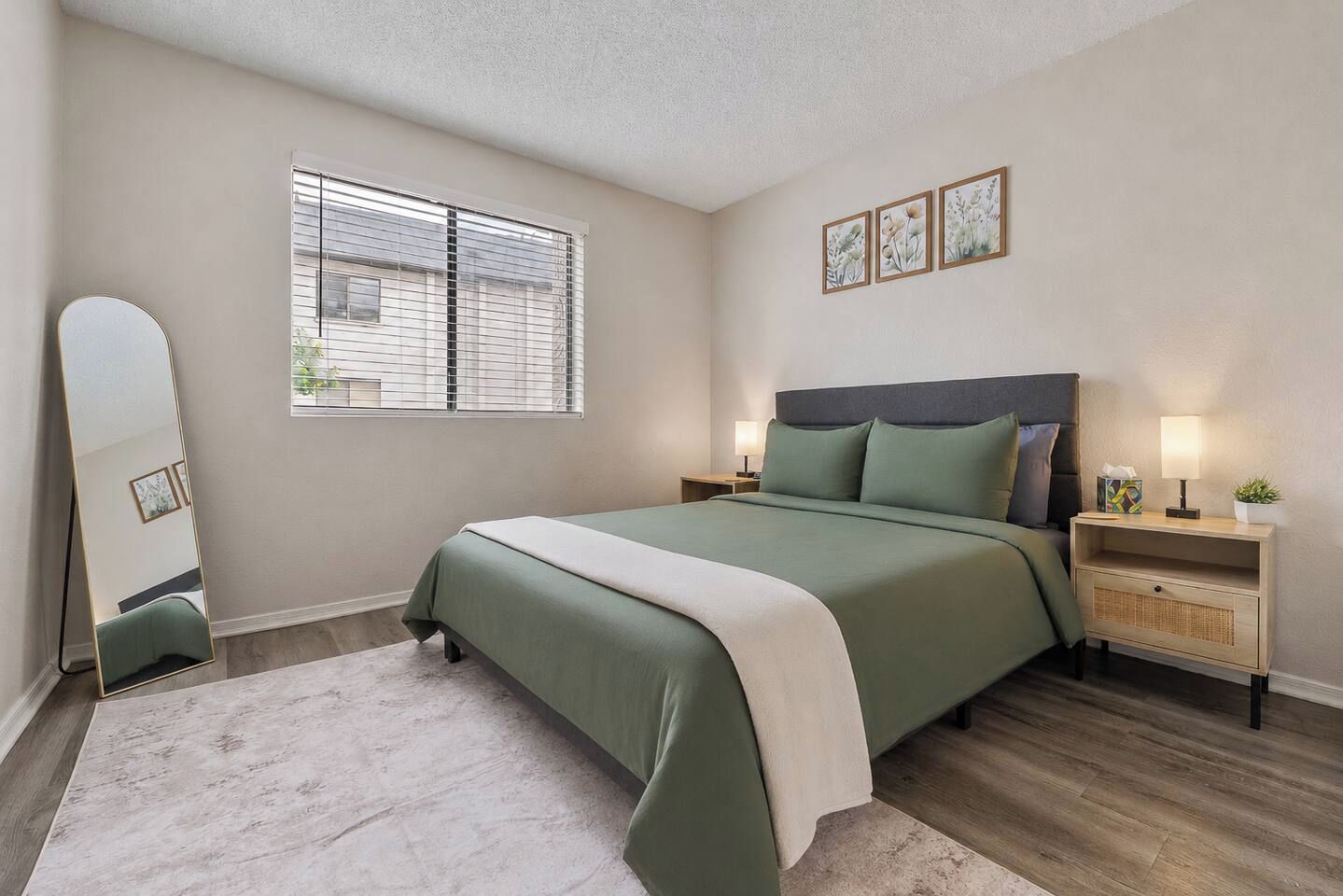 A bedroom with a bed, bedside tables, a mirror, and a window with blinds.