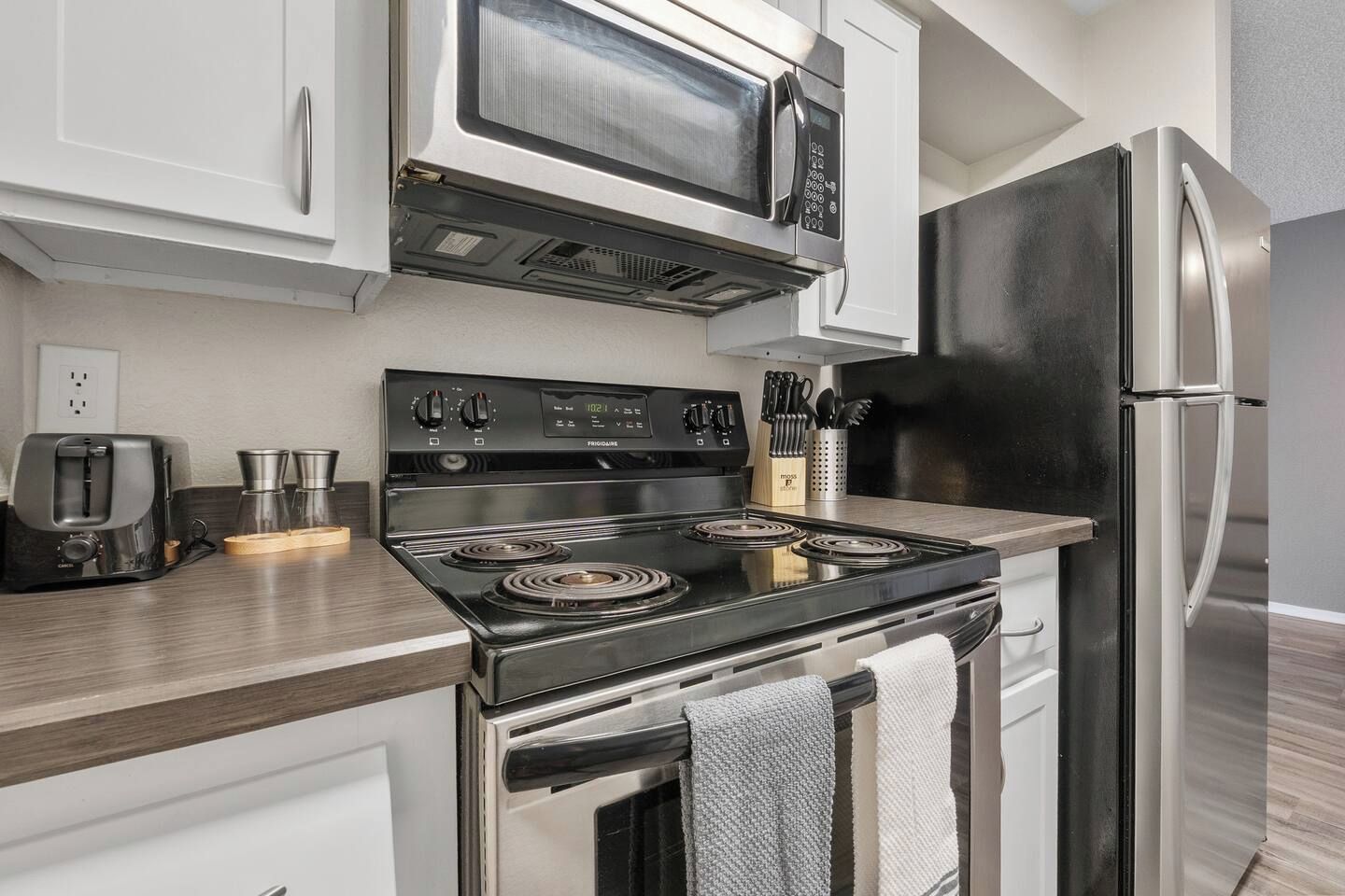 A modern kitchen with a stainless steel refrigerator, a built-in microwave, a stovetop with a digital control panel, and a toaster.
