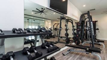 Un gimnasio con equipamiento de levantamiento de pesas, mancuernas y un espejo.