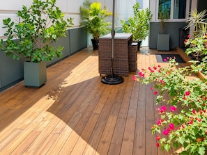 Eine Holzterrasse mit Blumentöpfen und einem Korbstuhl.