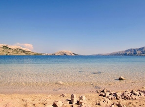 A clear beach with calm water, rocky foreground, and distant hills. - Two bedroom Apartment with Splendid View (Zubovići)