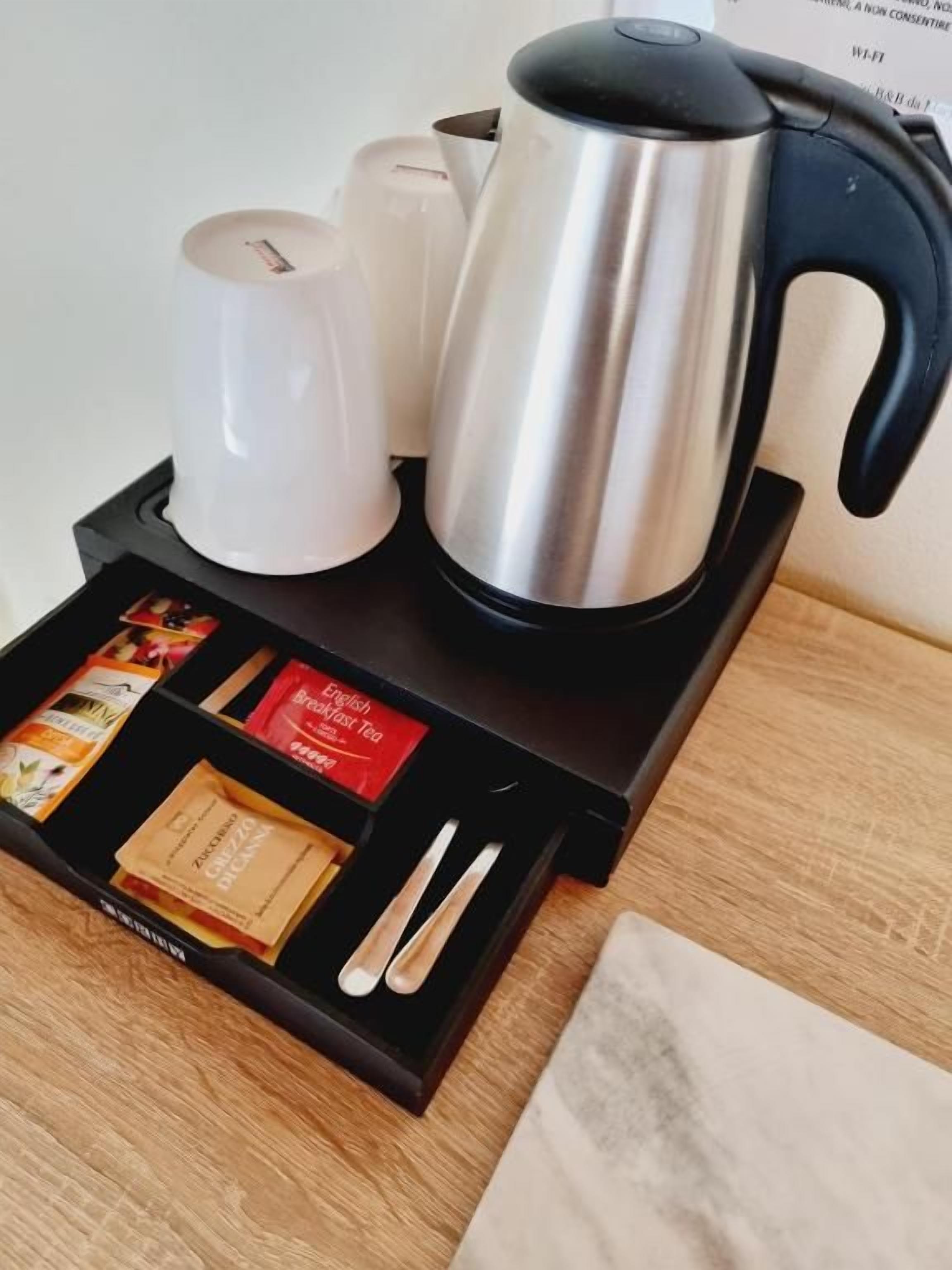 A coffee maker, two white cups, and a tray with tea bags and a spoon on a black tray.