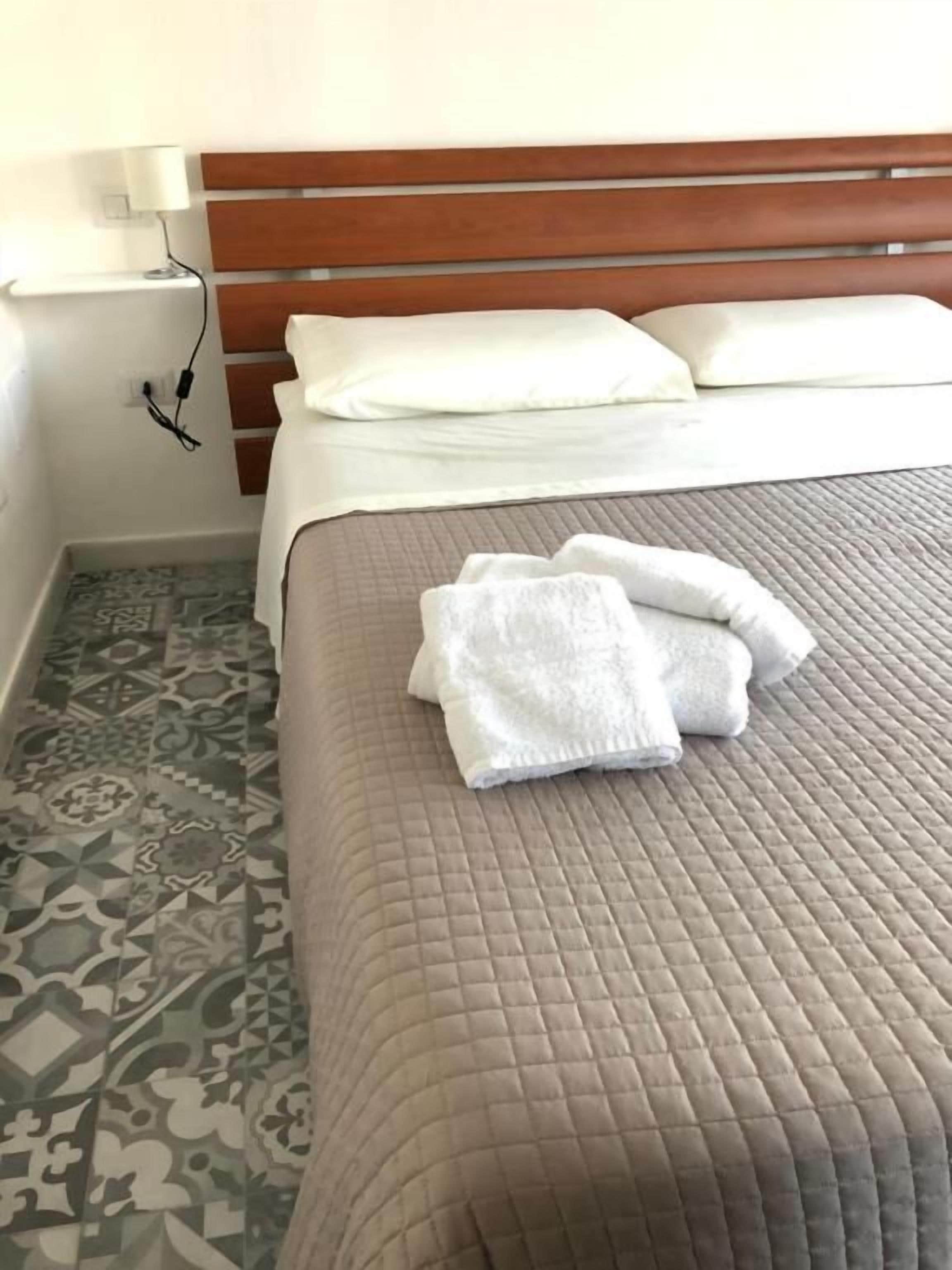 Un letto rifatto con un copriletto marrone, un cuscino bianco e un asciugamano piegato di colore bianco.