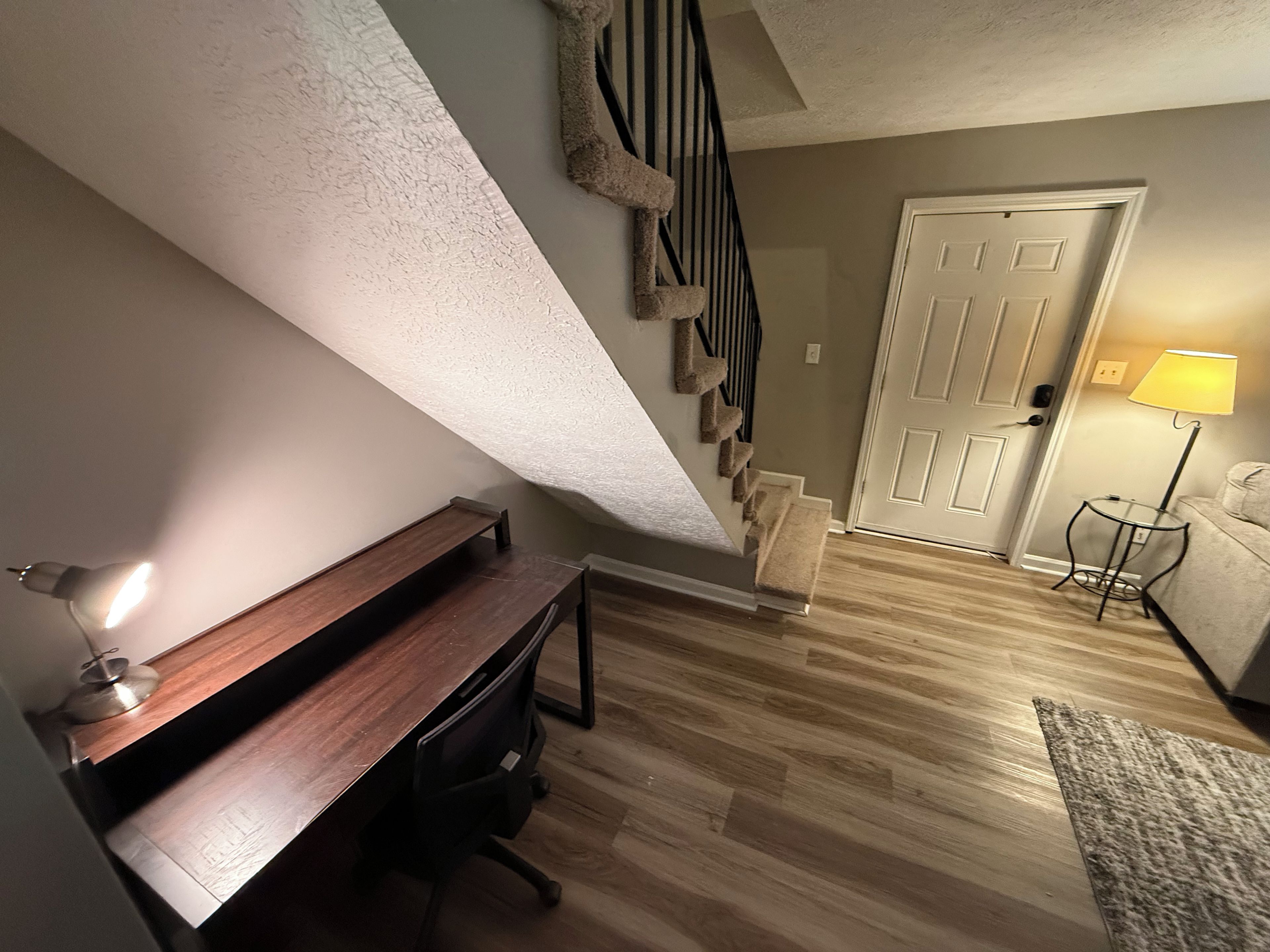 Ein Zimmer mit Schreibtisch, Stuhl, Treppe, Tür und Lampe.