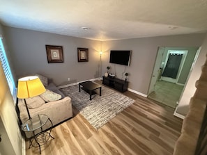 A living room with a sofa, coffee table, TV, and a small table with a lamp. - Cozy Rome Condo - Full Kitchen - Washer/Dryer -Great for Work Stays (Rome)