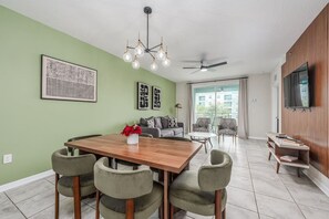 A modern living room with a dining area, a ceiling fan, and a TV mounted on the wall. - 2 Bedroom Condo in Top Resort - 5 Miles to Disney (Kissimmee)
