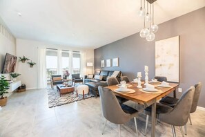 Ein modernes Wohnzimmer mit einer Couch, einem Couchtisch und einem Essbereich mit Stühlen und einem für eine Mahlzeit gedecktem Tisch.