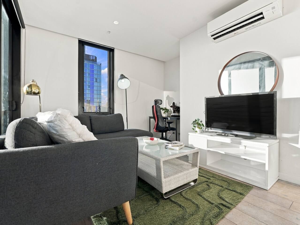 A modern living room with a sofa, a coffee table, a TV, and a large window with a city view.