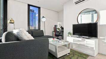 A modern living room with a sofa, a coffee table, a TV, and a large window with a city view.
