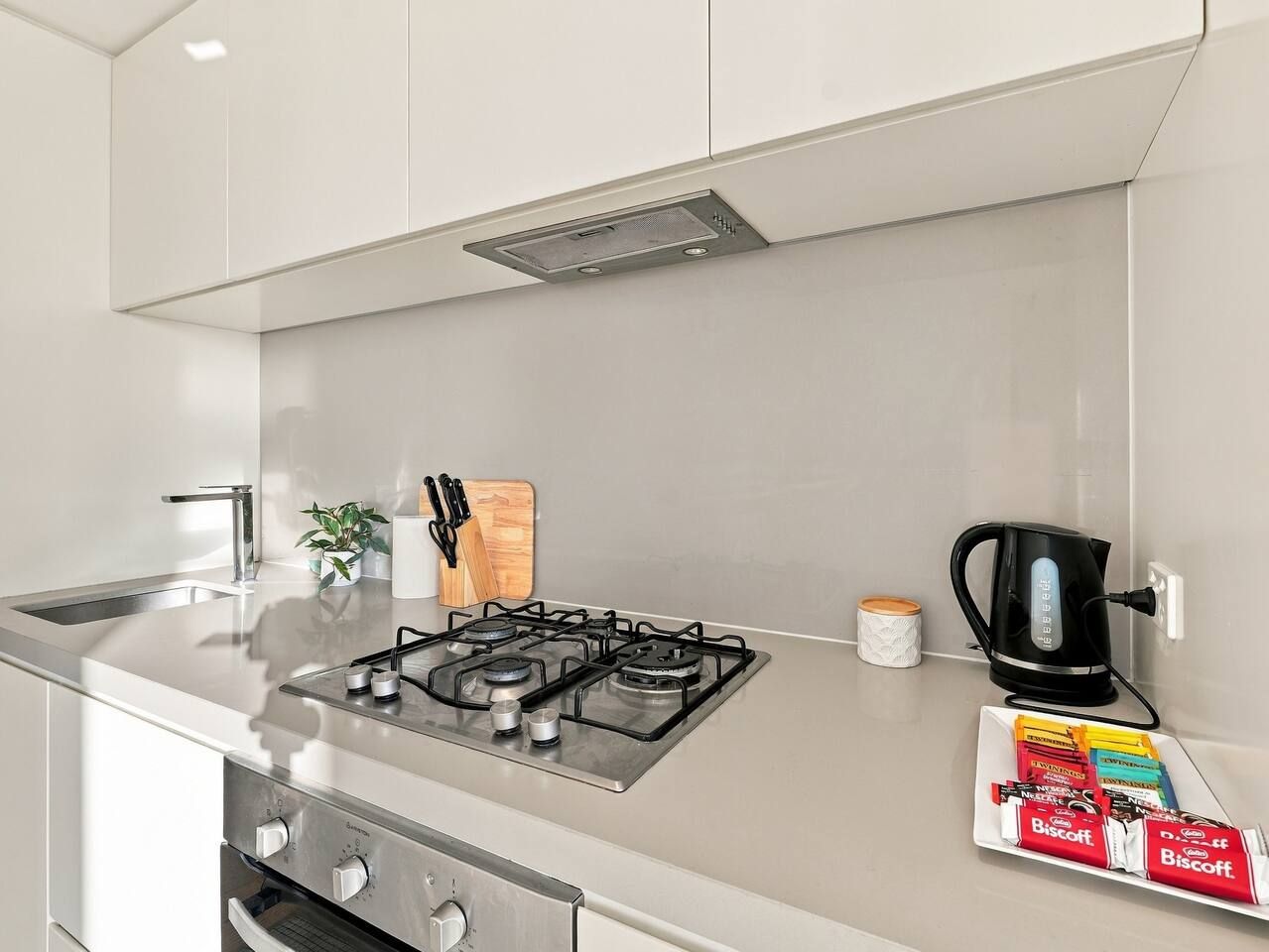 A modern kitchen with a gas stove, a coffee maker, and a box of Biscuits.