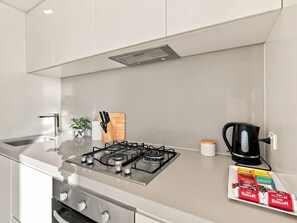 A modern kitchen with a gas stove, a coffee maker, and a box of Biscuits. - Melbourne CBD 2BR | Pool, Gym & City Views (Melbourne)