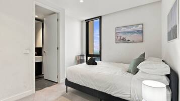 A bedroom with a bed, a nightstand, a lamp, a painting, and a view of the outdoors.