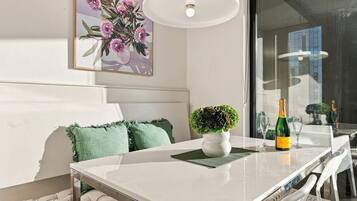 A modern dining area with a white table, green cushions, a small potted plant, and a bottle of champagne.