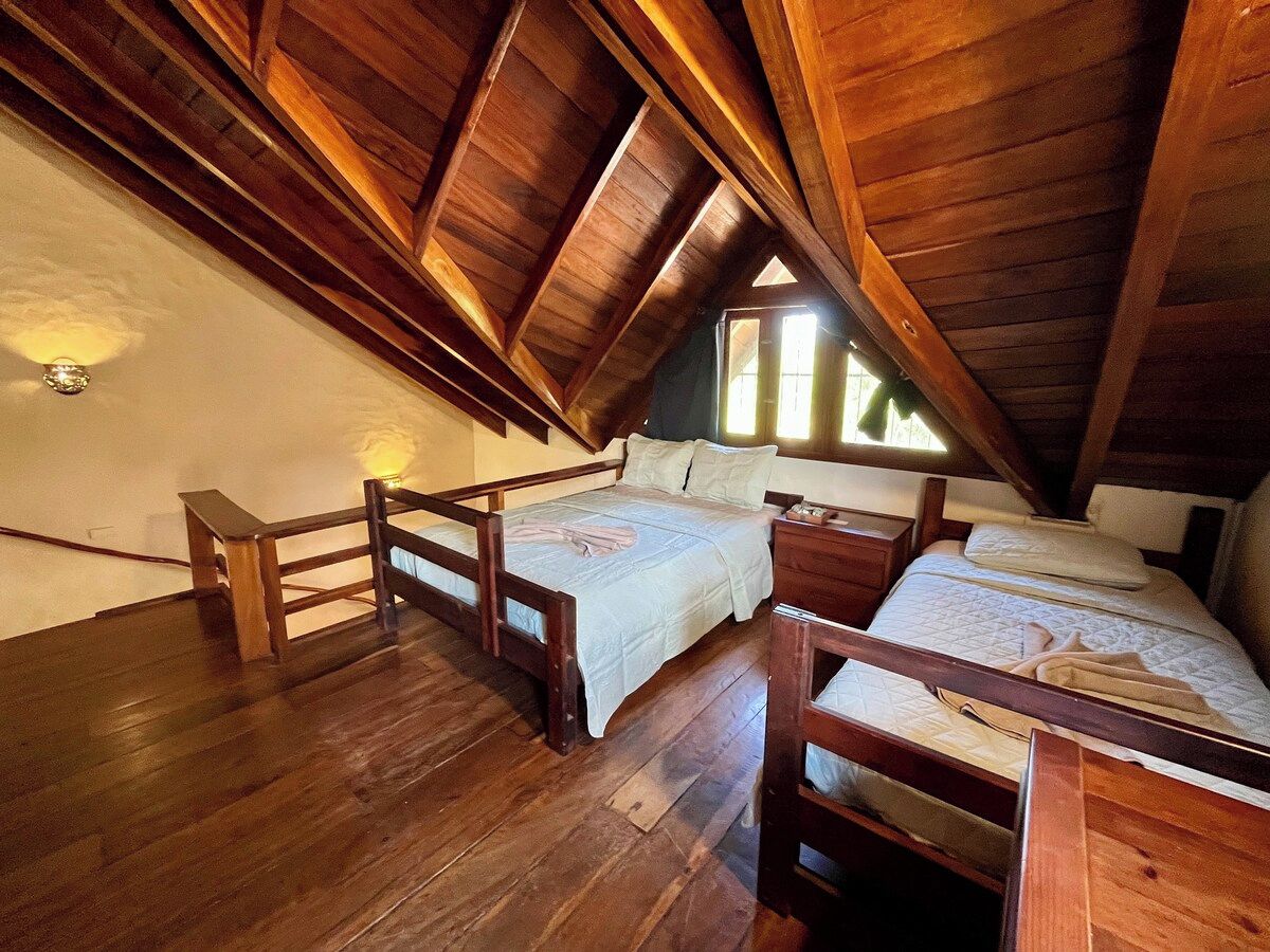 Une chambre à coucher aménagée dans un grenier, avec des poutres en bois, un plafond en pente et deux lits.