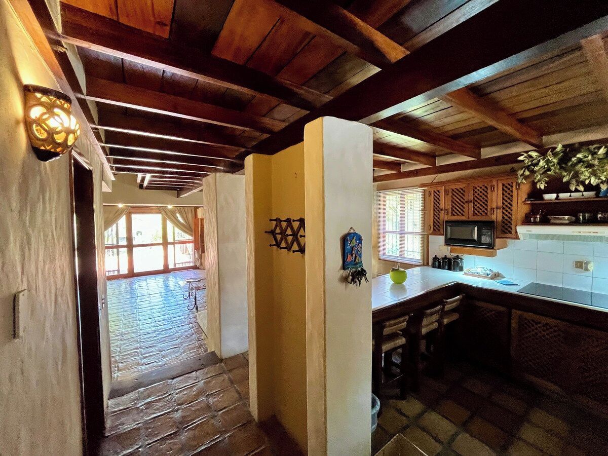 A rustic kitchen with wooden beams, a tiled floor, and a window with blinds.